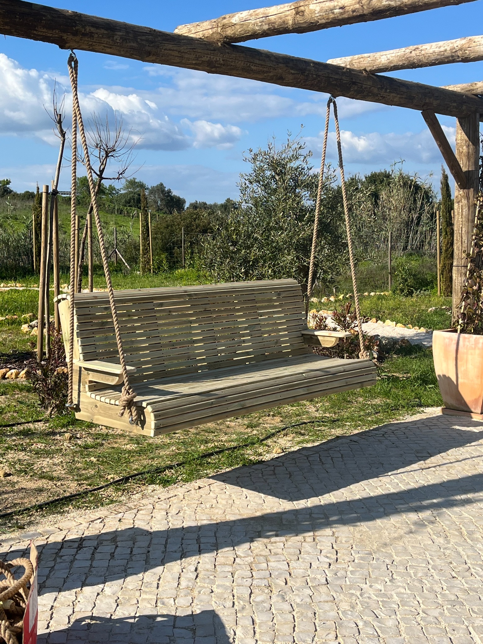 Timber hanging garden bench suspended with rope beneath a rustic pergola