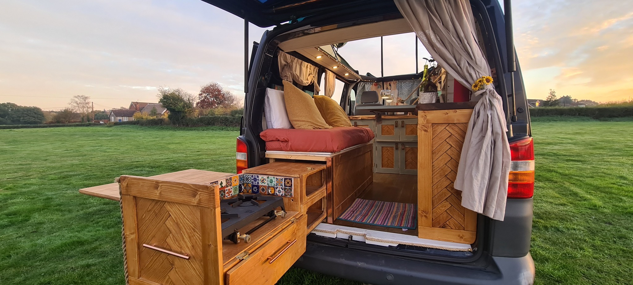 Completed campervan conversion with its pull-out rear kitchen open at sunset